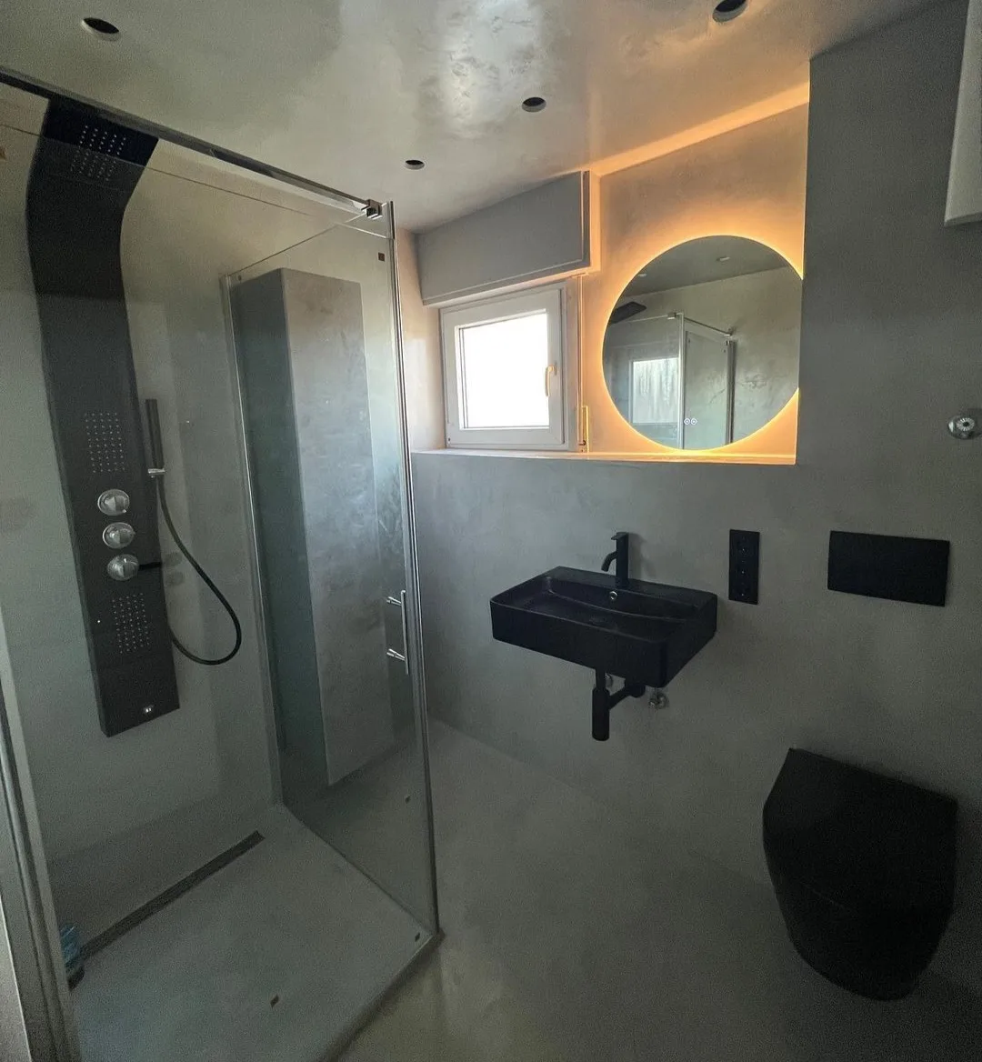 Fertig saniertes Designbad mit Walk-in-Dusche, beleuchtetem Rundspiegel und wandhängenden Objekten