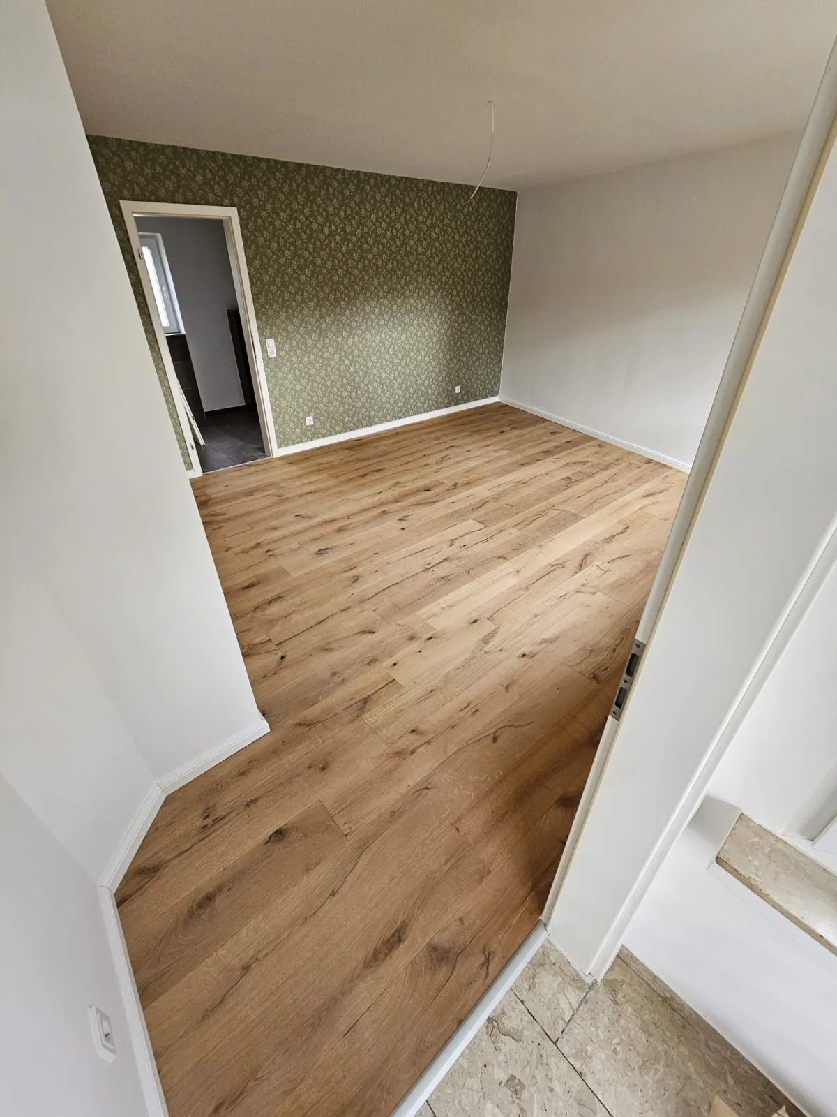 Derselbe Raum mit neu verlegtem Eichen-Dielenboden und weißen Sockelleisten nach der Bodenverlegung